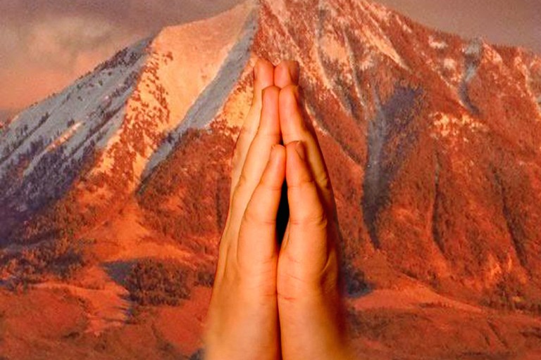 Praying hands raised against a glowing mountain.