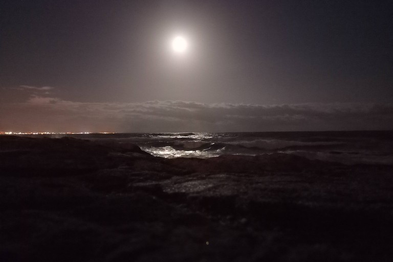 A full moon over dark ocean waves, its reflection scattered across the water.